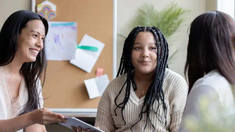 Three people talking in a casual indoor setting with a bulletin board and plant in the background. One is a prospective student meeting with educational study abroad agents.